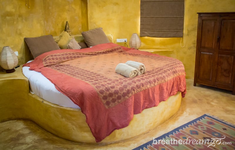 Round bed with pink cover in yellow stone room in Goa