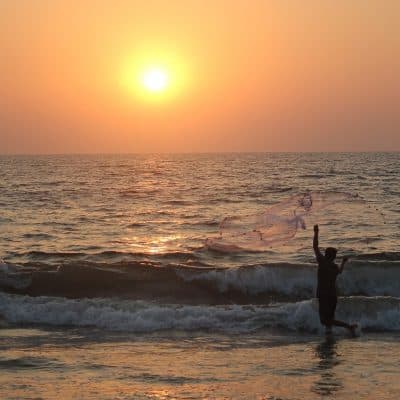 ocean at sunset with man throwing a net