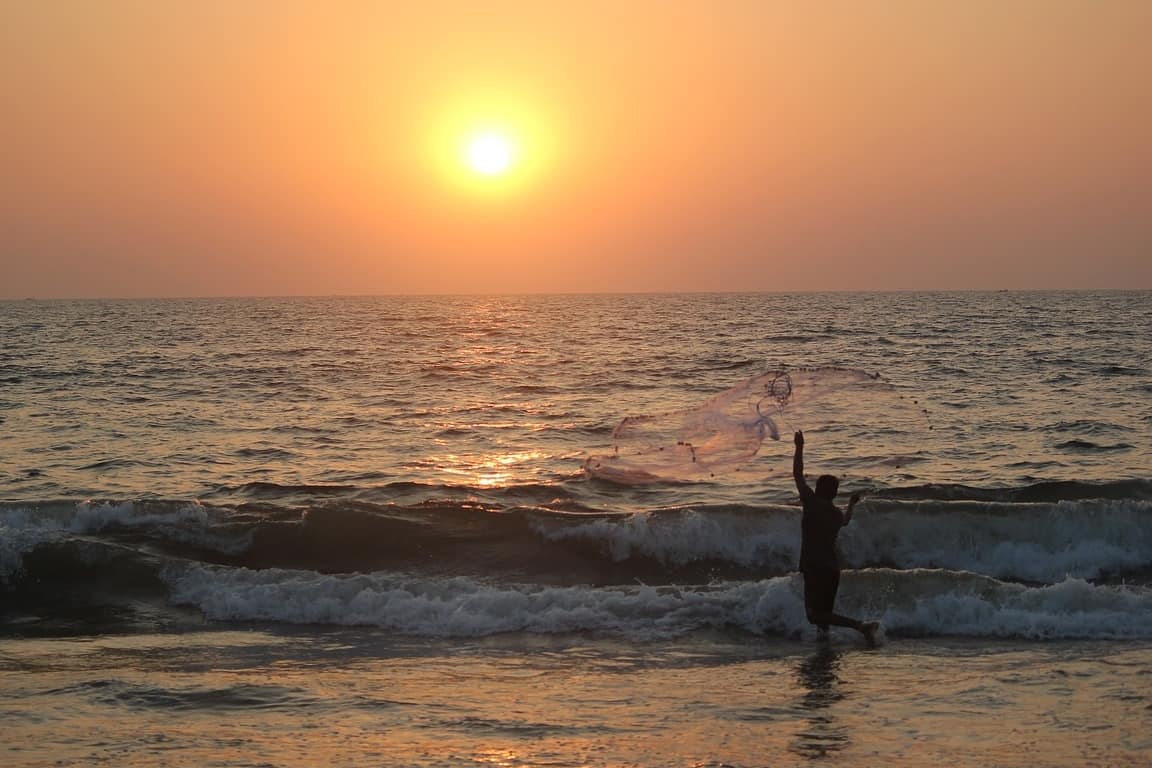 ocean at sunset with man throwing a net