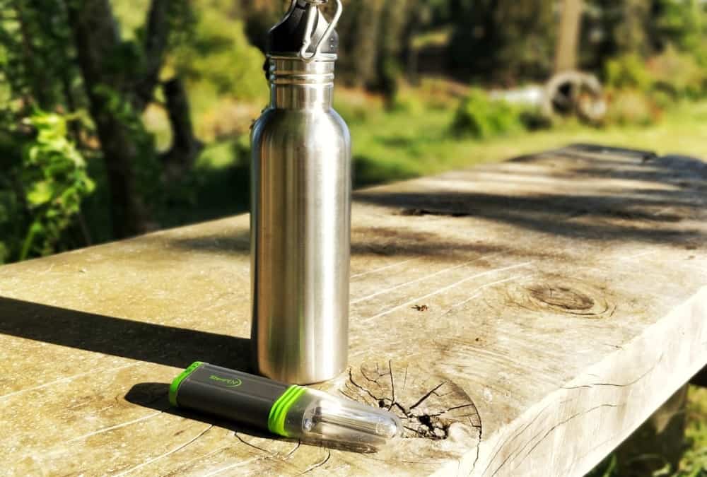 Steripen and water bottle on wooden bench in forest