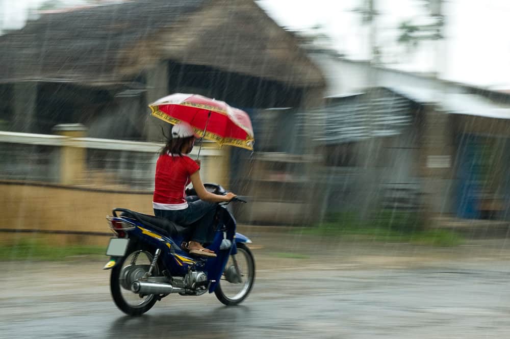 Woman in Vietnam rides a motorcycle while holding an umbrella